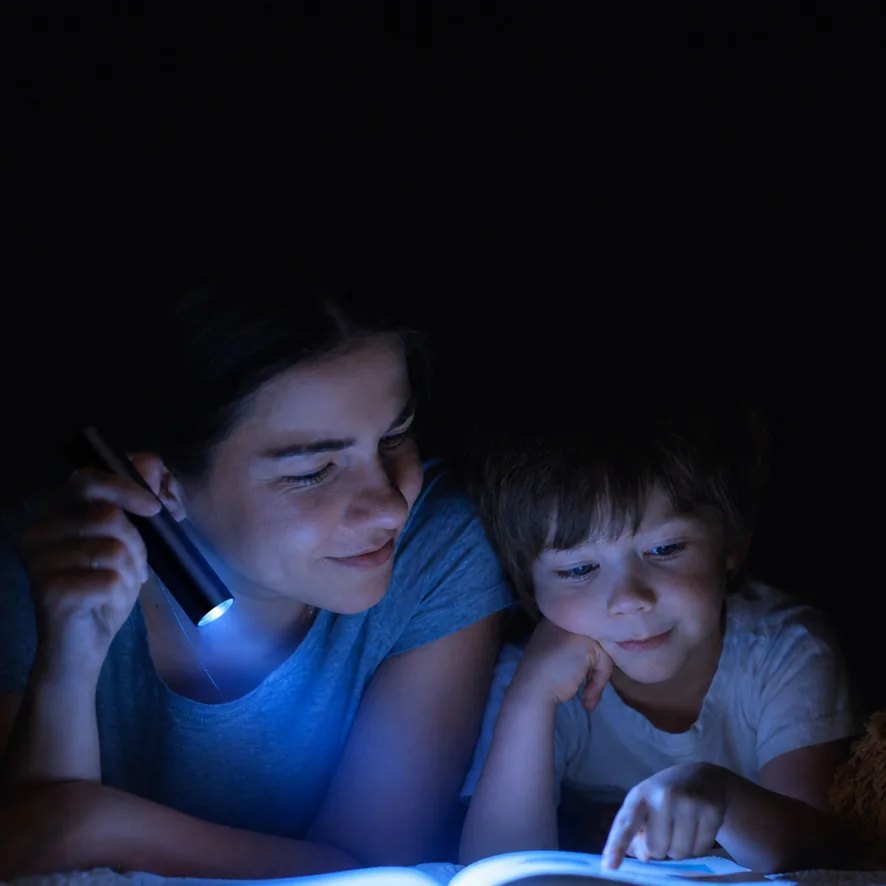 A mother and child sharing story time with a flashlight