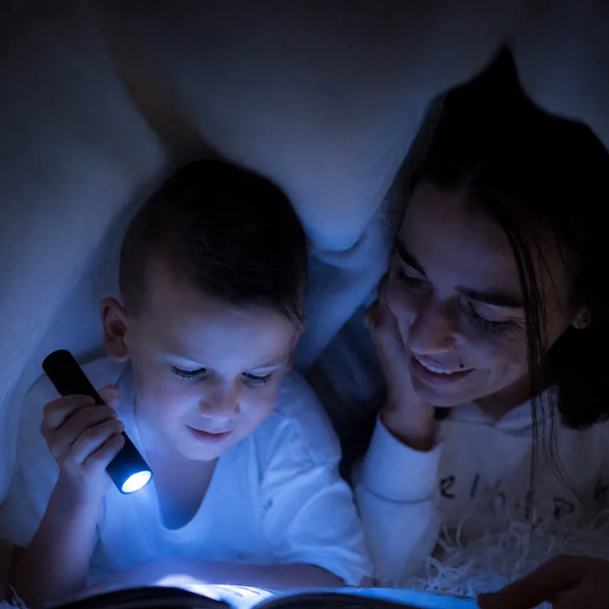 A child and mother reading together under a blanket